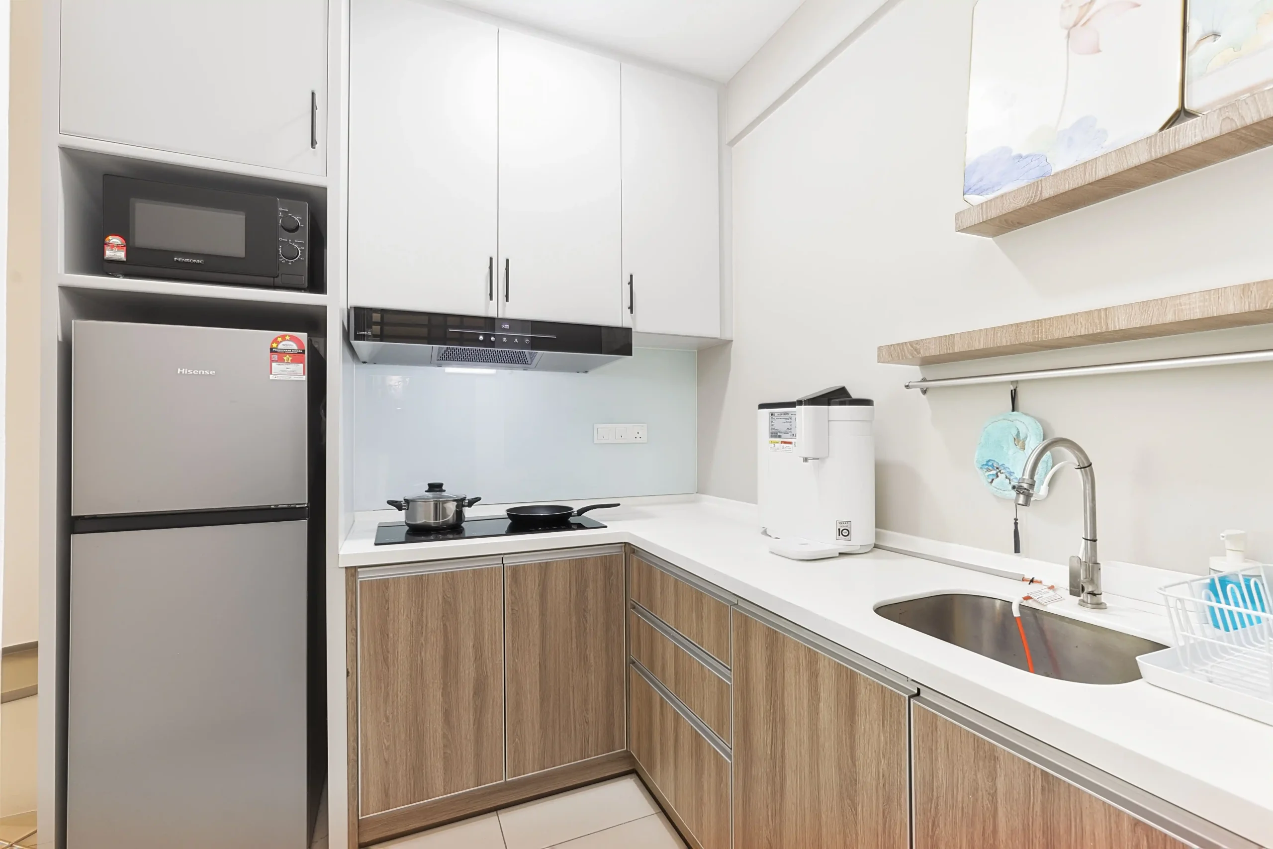 Kitchen setup equipped with refrigerator, microwave, electric stove, and kettle